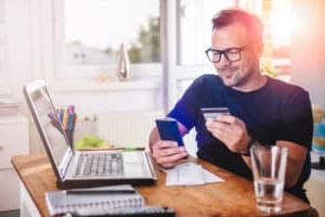 Young man at home office using credit card on his mobile phone